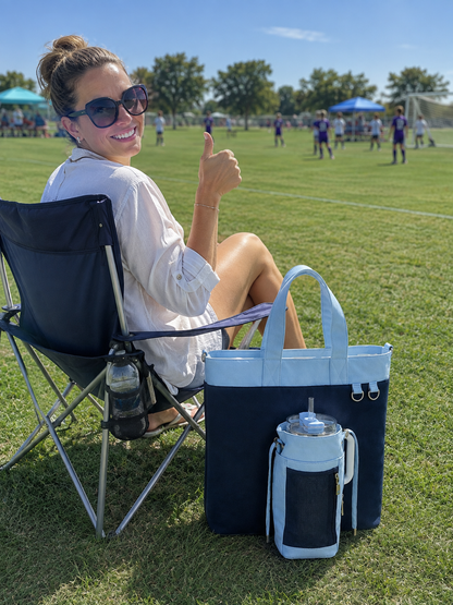 A mom is carrying a blue Water bottle tote bag at a soccer game with 40oz water bottle waiting for her son.